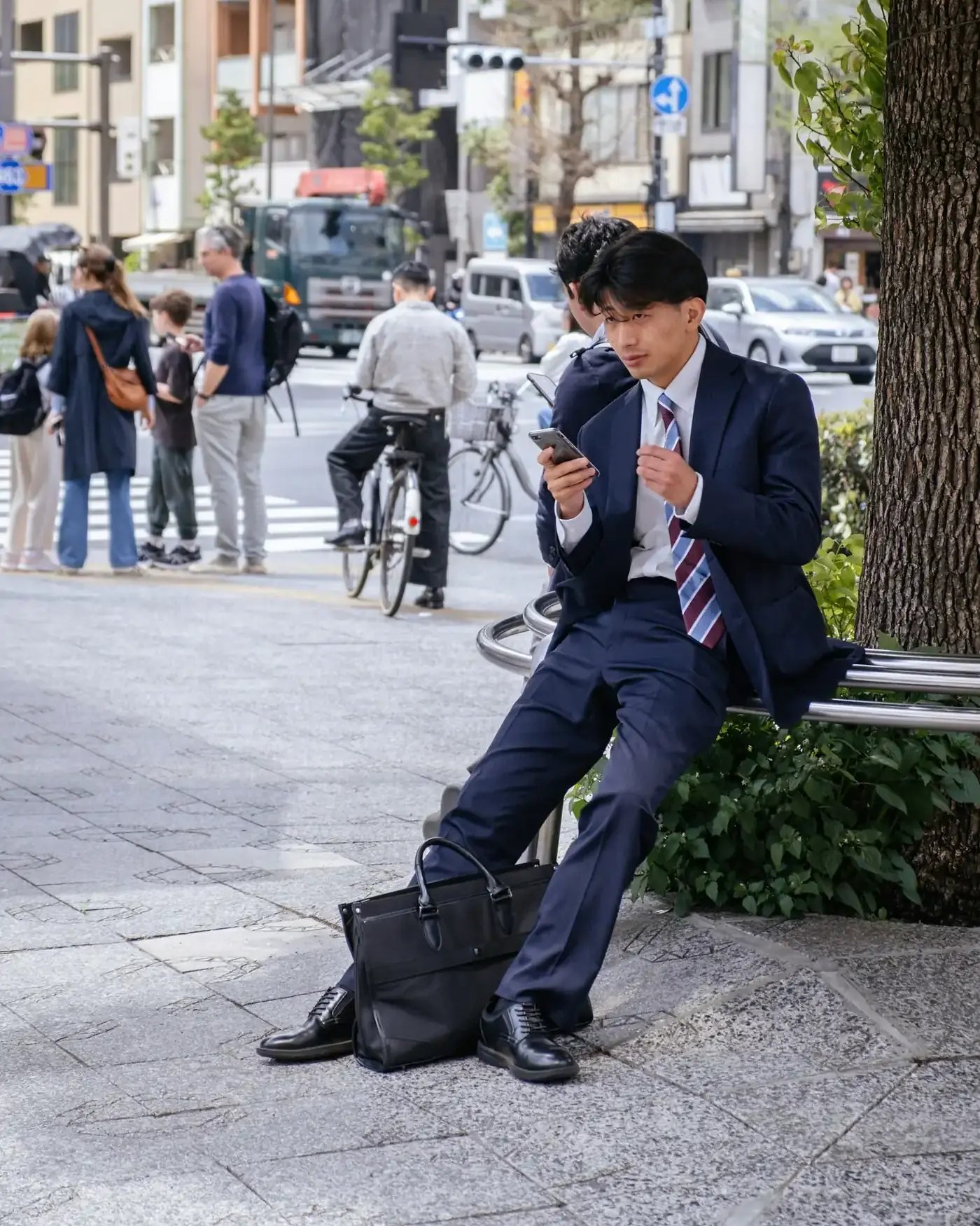 A businessman sitting on a bench in Osaka, looking at his phone