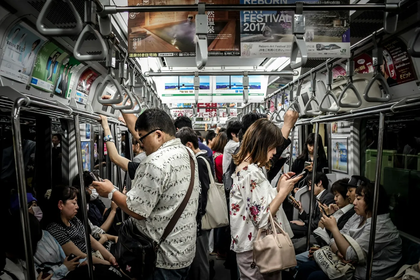 Passengers standing in a crowded Japanese train, looking at their phones